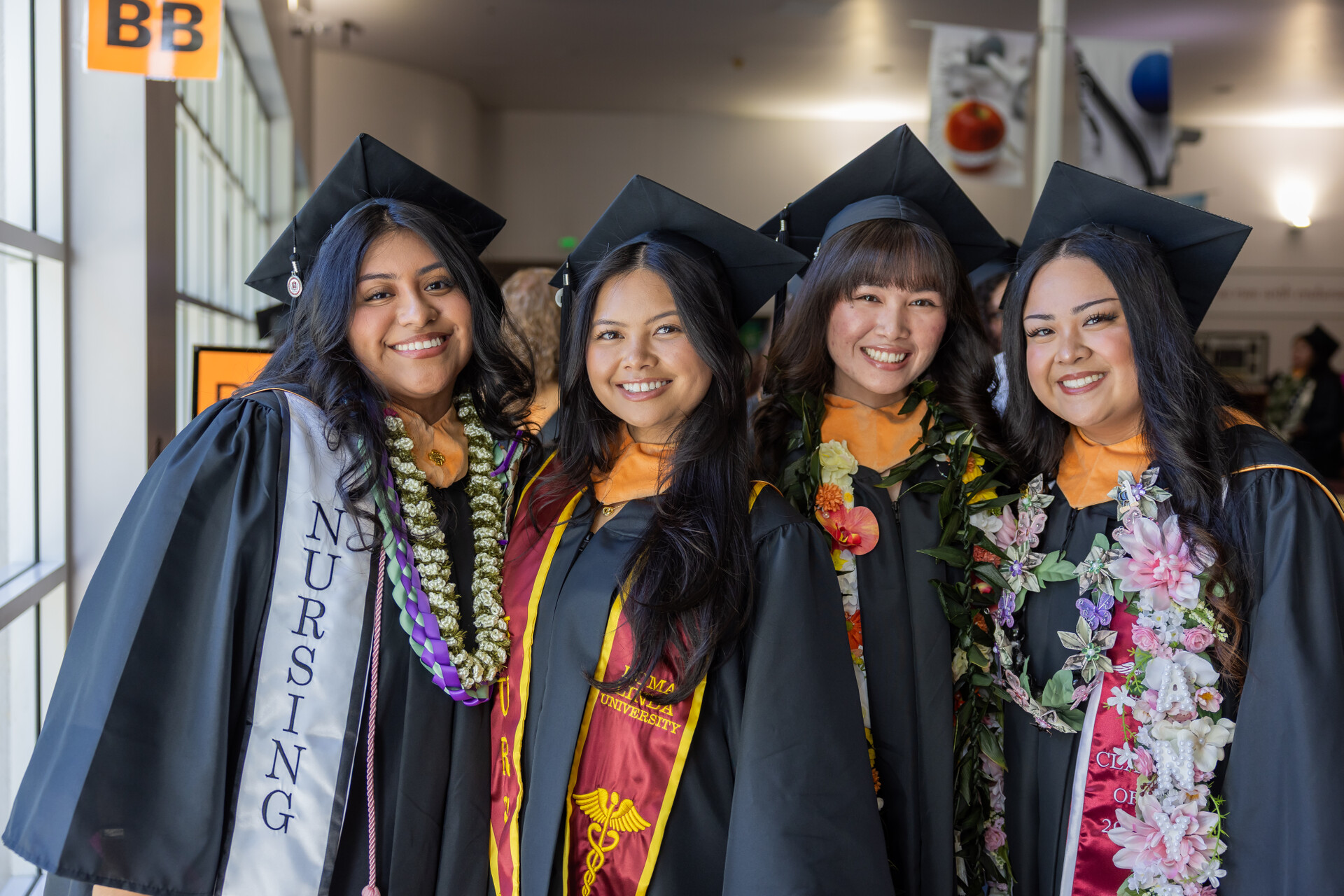 Four female nursing graduates stand together smiling in their caps and gowns. 