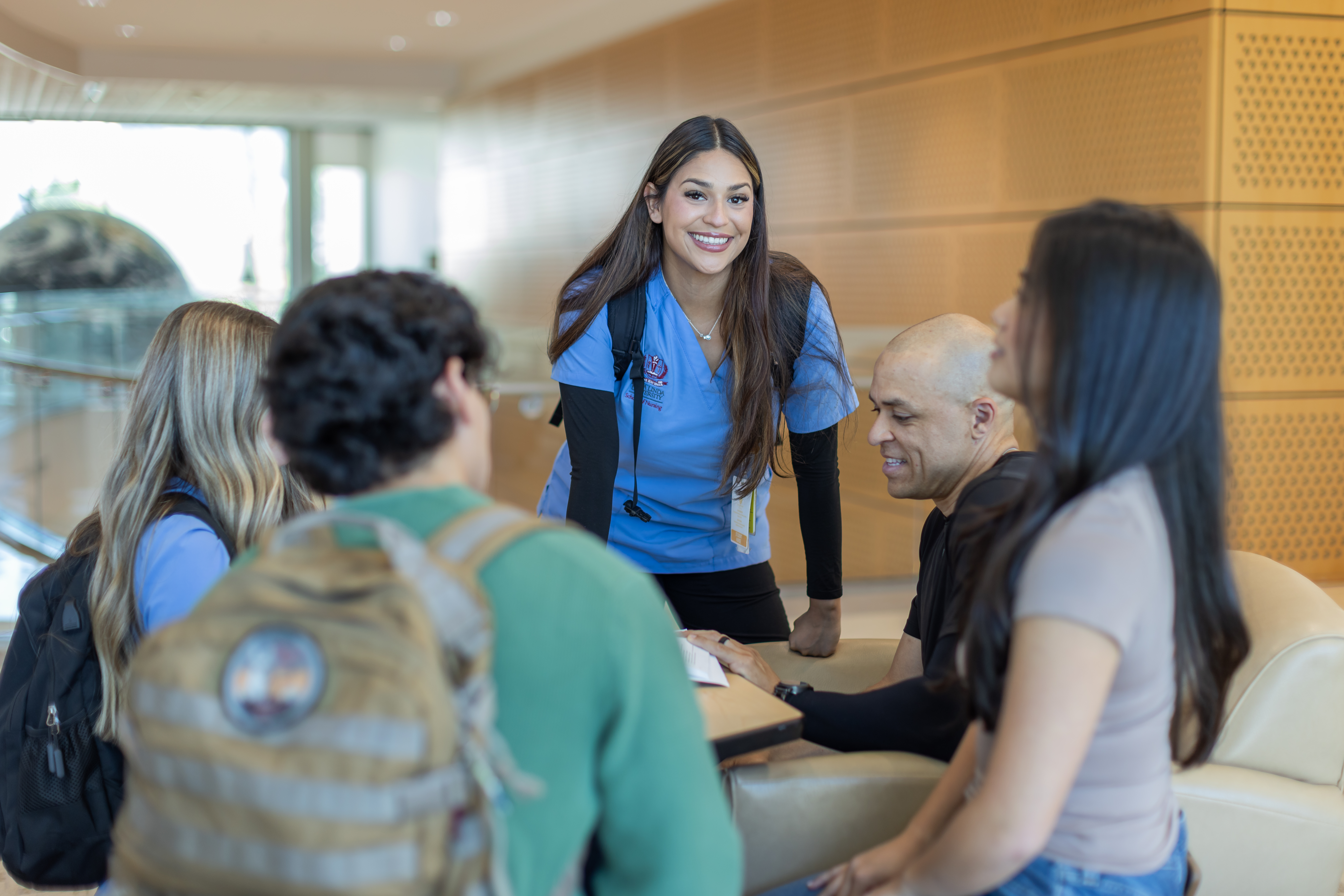 A female nursing student smiles as she stands next to a group of students having a conversation.