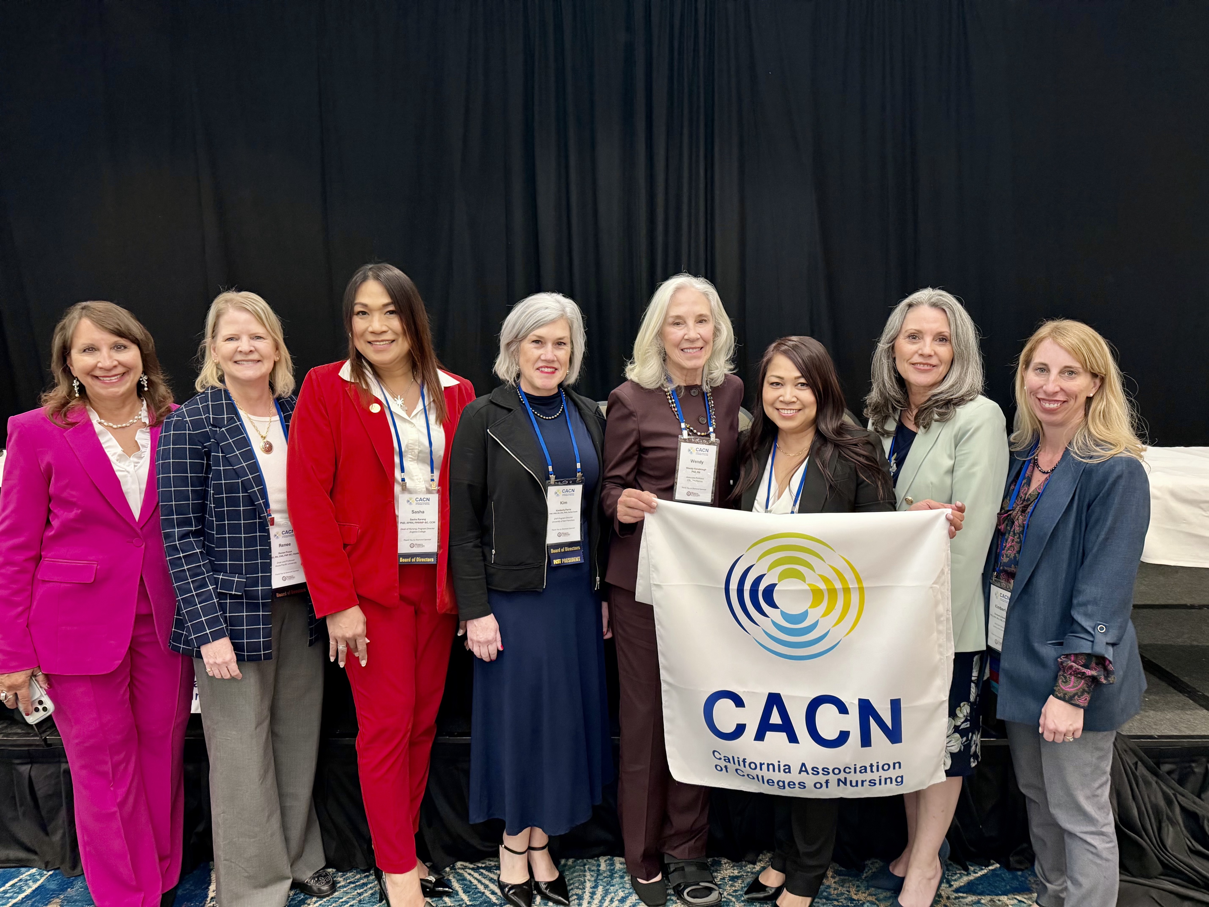 A group of healthcare professionals stand together at an event holding up a sign that reads "CACN." 