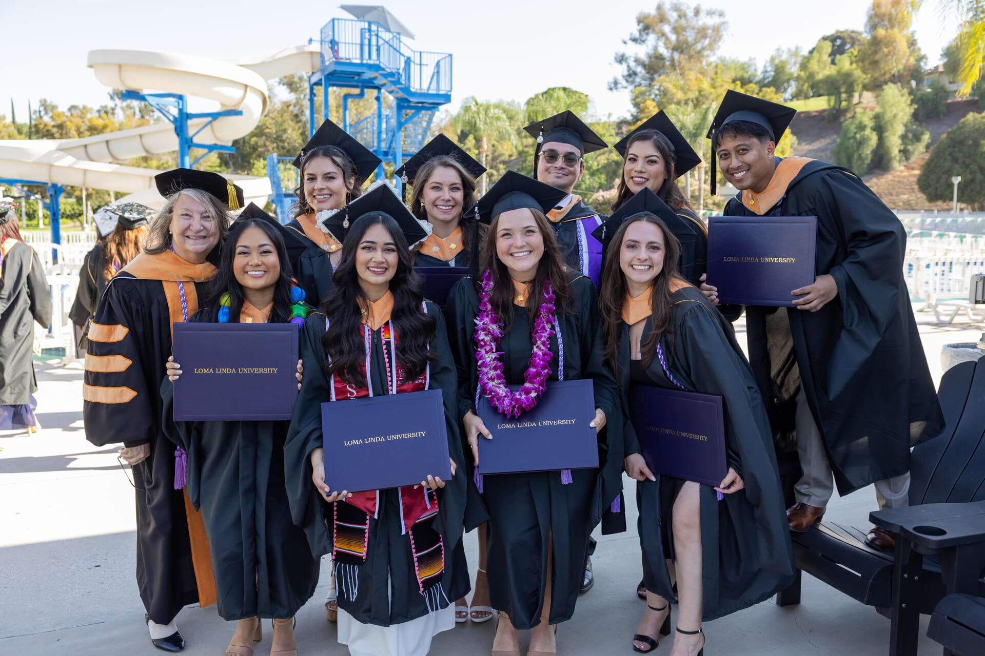 A group of graduate nursing professionals stand together holding their diplomas and celebrating after their commencement ceremony. 