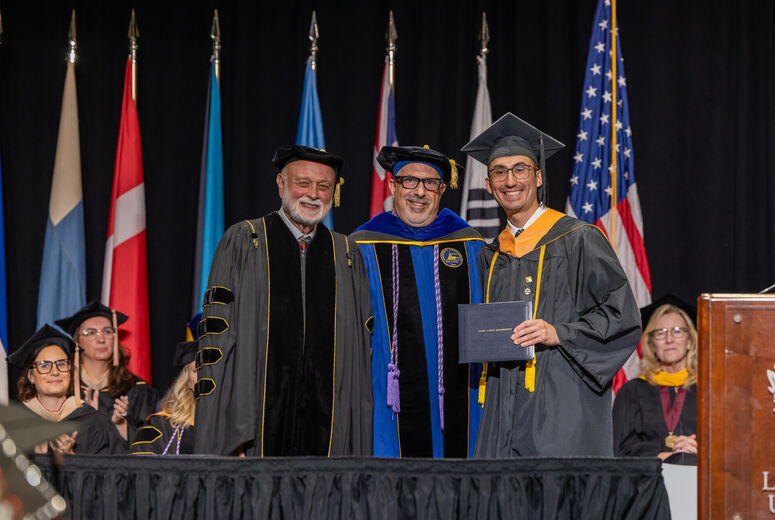 Male nursing student being presented with an award by two administrators. 