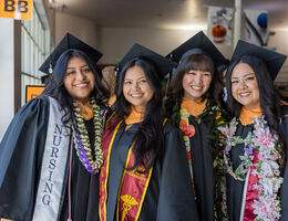 Four female nursing graduates stand together smiling in their caps and gowns. 