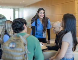 A female nursing student smiles as she stands next to a group of students having a conversation.