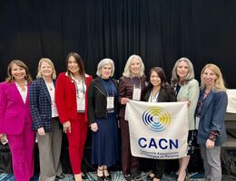 A group of healthcare professionals stand together at an event holding up a sign that reads "CACN." 