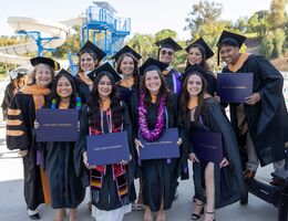A group of graduate nursing professionals stand together holding their diplomas and celebrating after their commencement ceremony. 